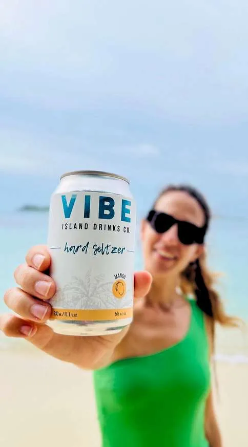 Smiling woman holding a can of Vibe on the beach