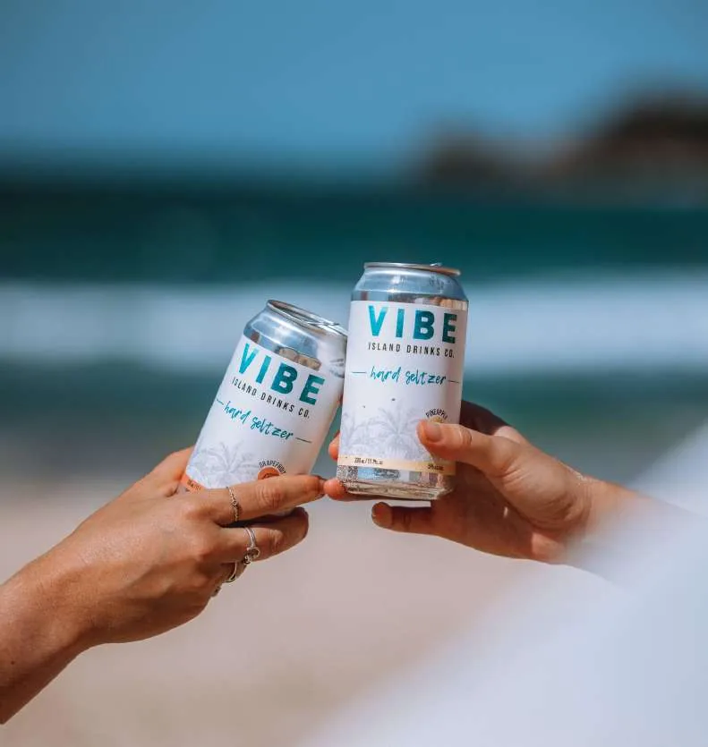 Two friends toasting with Vibe cans by the sea